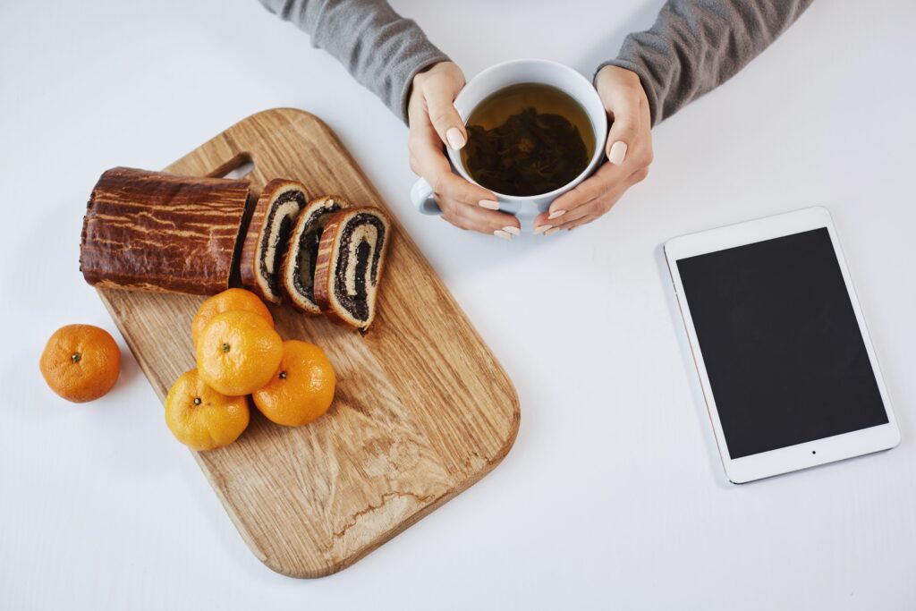 cup-tea-makes-morning-look-brighter-modern-woman-holding-pot-eating-tangerine-rolled-cake-breakfast-lunch-waiting-her-boss-send-her-information-via-digital-tablet