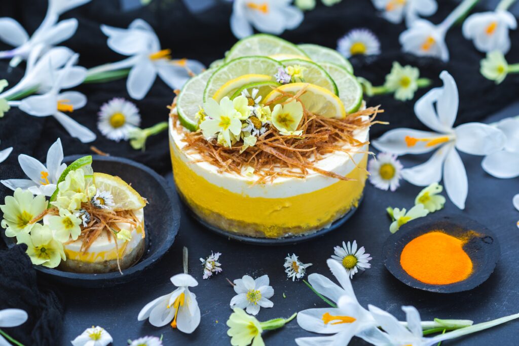 Raw vegan cake with lemon and lime on a black surface covered with tiny daisy flowers